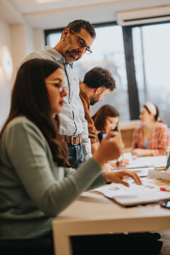 A dedicated team collaborates closely in an office setting, with a man overseeing a woman's work. The environment is studious yet relaxed, indicating effective teamwork and concentration.