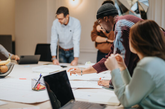 Business team actively engaged in a workshop, collaborating over documents and using laptops in a well-lit modern office environment.