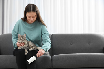 Pet shedding. Woman with lint roller removing cat`s hair from trousers on sofa at home, space for text
