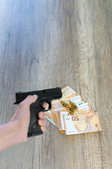 photograph of hand with gun pointing at table with many euro banknotes and bullets