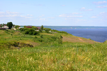 Fototapeta na wymiar grassy hill with cottages on the top and blue river coy space 