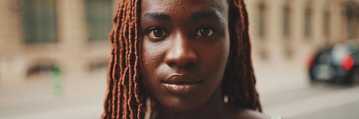 Close-up of beautiful woman with African braids raising her head and looking at the camera with...