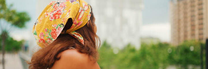 Profile of cute tanned woman with long brown hair wearing white top and yellow bandana stands...