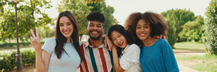 Happy, lovely multiethnic young people posing for the camera on summer day outdoors, Panorama. group of friends hugging each other smiling at the camera while standing on path in the park