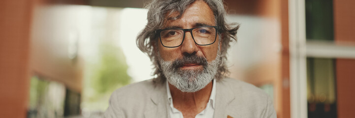 Clouse up, Panorama of mature businessman with beard in eyeglasses wearing gray jacket sits on cafe. Middle aged manager successful man user on laptop pc computer sit at cafe outdoors