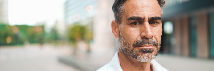 Close-up Businessman mature with neat beard wearing white shirt looks turns his head at the camera...