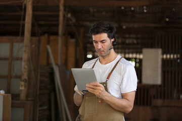 Portrait of male carpenter using digital tablet checking furniture at woodwork workshop. Male joiner working in furniture workshop. Start up and small business concept