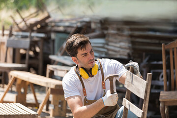 Male carpenter repairing wooden arm chair at woodwork workshop. Male joiner working in furniture...