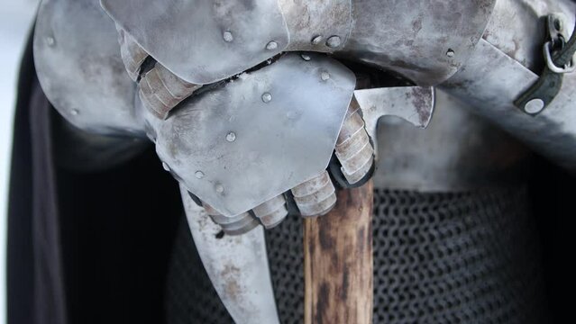 Close-up of the hands of a medieval warrior in plate gloves against the backdrop of a winter forest. Camera movement, selective focus.