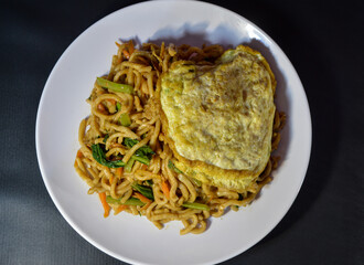 Mie goreng or fried noodles is one of the most popular foods in Southeast Asia, including Indonesia. Served with crackers, eggs and vegetables, on a plate.