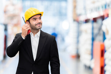 American male manager, engineer position Looking at merchandise in a warehouse, holding a radio, wearing a hard hat and suit. In industrial plants regarding plastic and steel business