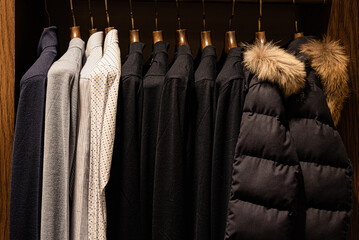 wardrobe with men's clothes in dark colors. jacket, down jacket, shirt. The clothes are neatly hung on wooden hangers