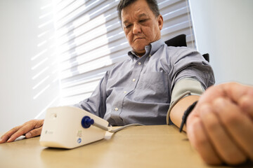 Asian man in 50s checking blood pressure with instrument in the work office