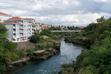 Fototapeta na wymiar Pedestrian bridge in Mostar over Neretva river, cityscape