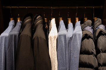 wardrobe with men's clothes in dark colors. jacket, down jacket, shirt. The clothes are neatly hung on wooden hangers
