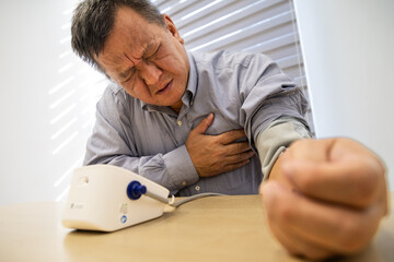 Asian man in 50s with painful chest checking blood pressure with instrument in the work office
