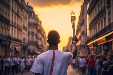 Ingelijste posters An unidentified man in a white t-shirt with a torch on the streets of Paris at sunset. Paris is the capital of the 2024 Olympic Games. Walking with the Olympic flame through the streets of Paris © Oleh