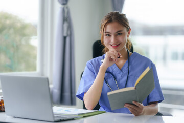 Attentive nurse in scrubs reviewing medical history or patient information on her laptop in office..