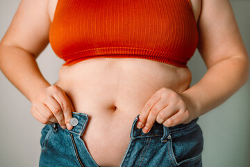 Fat woman trying to zip up her jeans pants. Women's health. Women body fat belly. Obese woman hand...