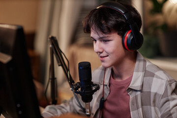 Portrait of smiling teenage boy playing video games online on PC computer with wireless headset and speaking to microphone