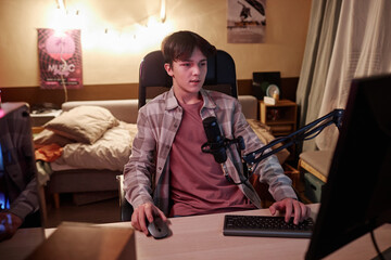 Wide angle view of teenage boy speaking to microphone while live streaming videogames and streaming
