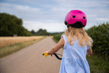 Fototapeta na wymiar Little child girl in a helmet rides a bike in a field