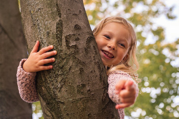 Smiling blond girl child points finger while lying on a tree