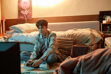 Portrait of teen boy holding gamepad and playing videogames sitting on floor at home, copy space © Seventyfour