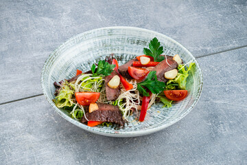 Slices of fried beef fillet steak with noodles, sweet peppers, tomatoes, lettuce, garlic and parsley.