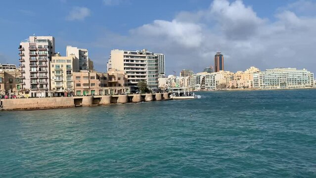 St Julian's city skyline. Motion of cars traffic and pedestrians. Mediterranean sea waves at Balluta bay. St Julian's, Malta 