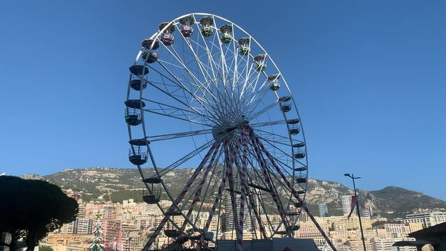 Motion of Christmas market ferris wheel installed next to the Port Hercule. Monaco city skyline and mountains in the background. Monaco, Cote d'Azur