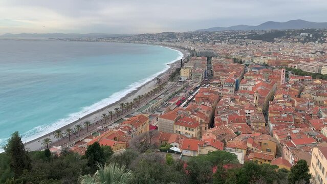 Nice city skyline. Panoramic, scenic aerial view. Motion of sea waves. Cars are moving on Promenade des Anglais. Red rooftops of Vieux Nice houses. Nice, Cote d'Azur, France