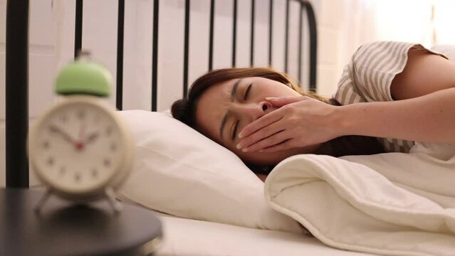 Asian woman yawn suffer from insomnia on her bed with a clock on bed side