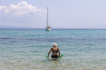 elderly woman swimming in the sea towards a yacht
