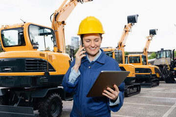 Engineer in a helmet with a digital tablet stands next to construction excavators