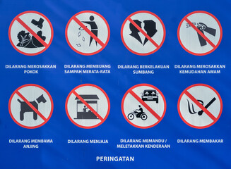 A poster in a park prohibition signs, not to litter, smoke, drive cars or motorbikes, light fires, bring dogs into the park, step on the grass, or engage in grocery shopping or couples activities