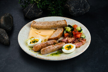 Traditional English breakfast sausages, bacon, eggs, cheese, vegetable salad, bread and sauce in plate.