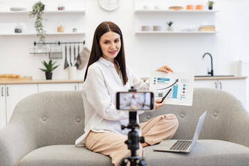 Intelligent professor showing currency growth graph to students during live streaming. Enthusiastic young caucasian female lector teaching financial literacy via video link on cell phone.