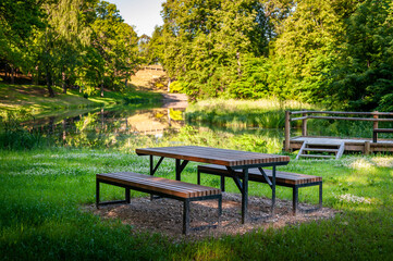 Wooden picnic tables near a river in Smiltene Old Park. Latvia. Recreational, picnic rest area in a park.