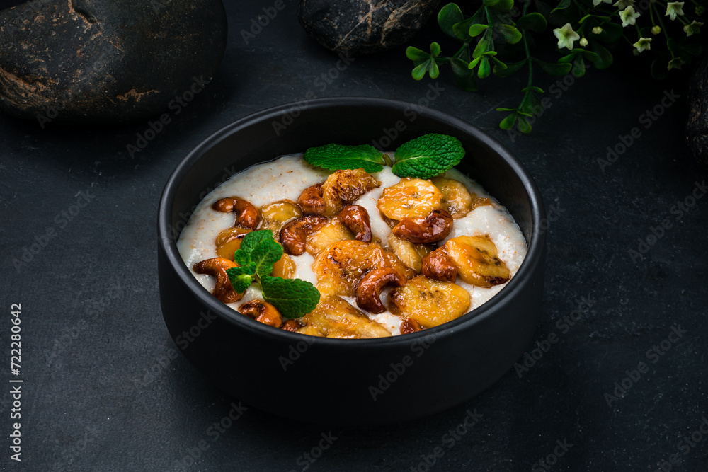 Poster Boiled oatmeal with fried bananas, cashews and mint in bowl.