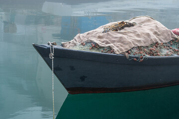 Grado, Italy - January 28th, 2024: a small fishing boat with fishing nets on the bow in the Mandracchio port on a winter day with thick fog.