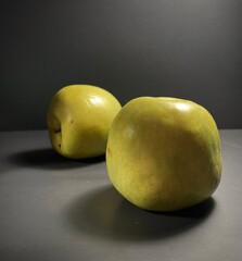 Two golden apples in a moody light, casting soft shadows on a dark background, evocative of autumnal still life scenes.