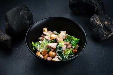 Fresh salad with chicken, lettuce, beans, croutons in bowl on a dark table.