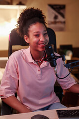 Portrait of smiling Black teenage girl speaking to microphone while recording podcast