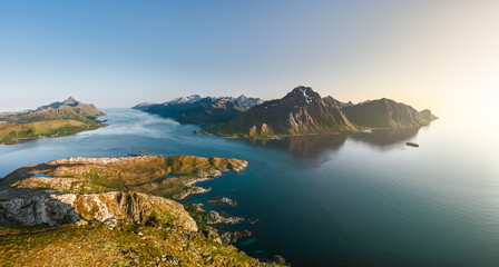 A panoramic view of the Lofoten archipelago under the midnight sun, with rugged peaks flanking the...