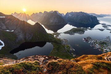 Sunset casts radiant light over Reinebringen, with the sun mirroring on calm fjord waters, the...
