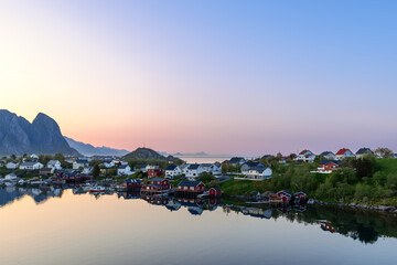 The calm waters of Reine, Lofoten Islands, under a pastel sky, reflect the picturesque village and...