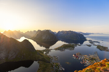 Midnight sun softly dips towards the horizon, a breathtaking view from Reinebringen unfolds, with...