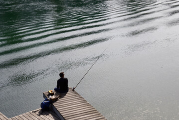 Geneva, Switzerland, Europe - single man rod fishing from Rhone river, leisure on river shore, peaceful spring day - obrazy, fototapety, plakaty