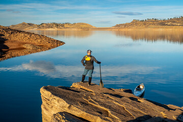 male canoe paddler with a paddle on  a rocky shore of a mountain lake - Horsetooth Reservoir in...